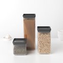 Trois boîtes de conservation à couvercles noirs, remplies de lentilles, spaghettis et pois chiches, à côté d'une tête d'ail.