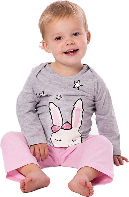 Un jeune enfant est assis par terre dans un haut de pyjama gris à imprimé lapin et un pantalon de pyjama rose.