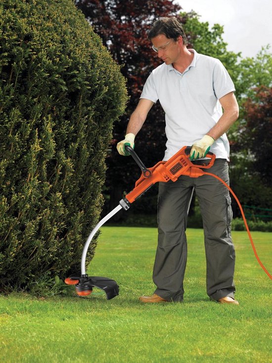 Man met oranje Black+Decker grastrimmer snoeit een struik.