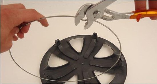 Hand met een tang die een metalen ring doorknipt die boven een zwarte wieldop ligt.
