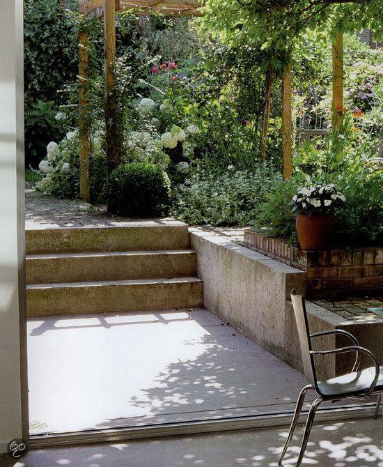 Terras met betonnen trap, bloempotten en een metalen stoel in een weelderige tuin.
