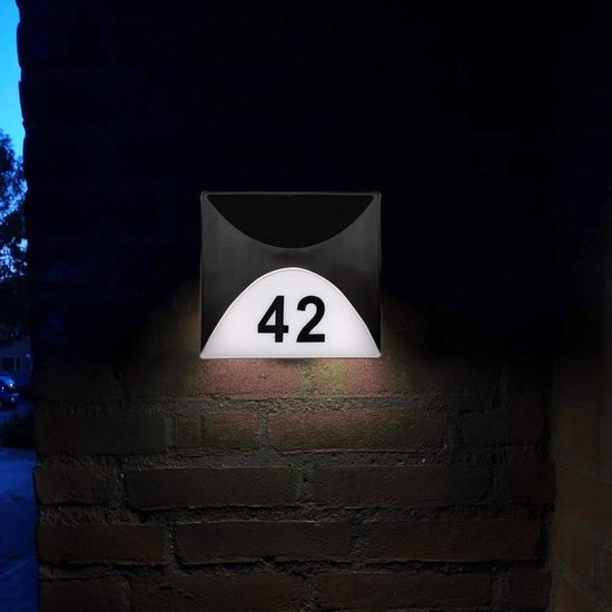 Huisnummer 42, zilverkleurig, verlicht op een bakstenen muur.