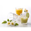Trois verres, deux remplis de jus. Un verre vide repose sur le côté. Avec des fleurs et des feuilles vertes.