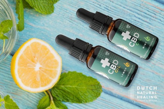 Twee flesjes CBD-olie van Dutch Natural Healing, een citroenpartje en muntblaadjes op een houten achtergrond.