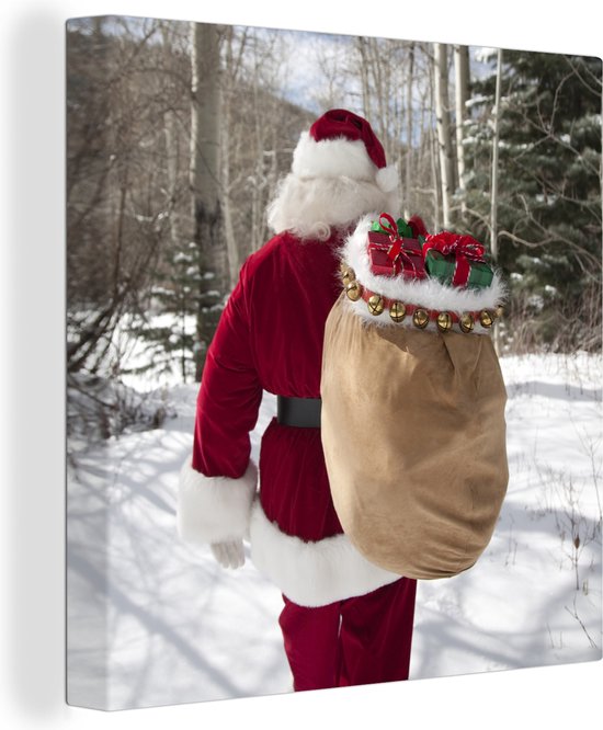 Canvas Schilderij De kerstman loopt met een zak vol met kerstcadeaus door een bos - 20x20 cm - Wanddecoratie