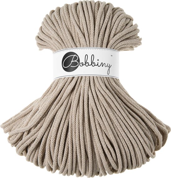Een rol Bobbiny beige macramé garen van 5mm, met een papieren wikkel met logo.