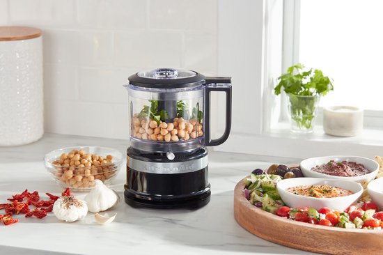 Zwarte KitchenAid hakmolen met kikkererwten in de kan, op een aanrecht met mezze.