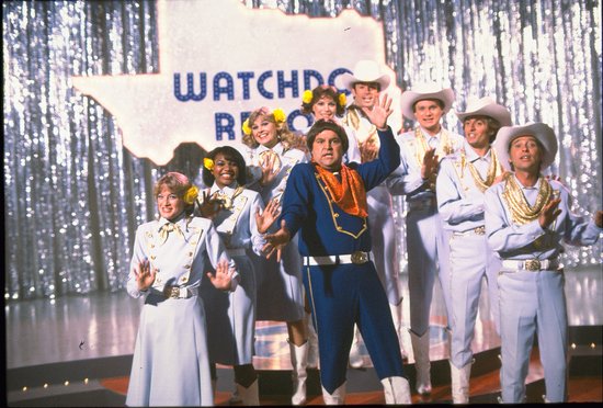 Groep mensen in westernkleding op een podium met een banner 'WATCHDOG REVENGE'.