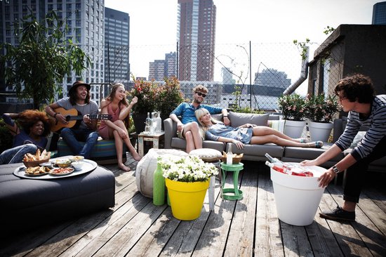 Groep vrienden op dakterras, met zitmeubels, planten en een grote witte koelbox.