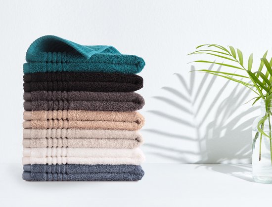 Une pile de serviettes de différentes couleurs avec une plante en arrière-plan.