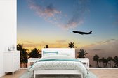 Behang - Fotobehang Silhouet van een vliegtuig boven de palmen - Breedte 390 cm x hoogte 260 cm