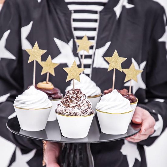 Een persoon met een zwart-wit sterrenjas serveert cupcakes met gouden sterprikkers.