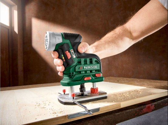 Hand van een persoon houdt een groene en zwarte Parkside accuschroefmachine vast die op een houten plank werkt.