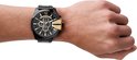 Mannelijke pols met een zwart Diesel horloge met goudkleurige accenten en metalen band.