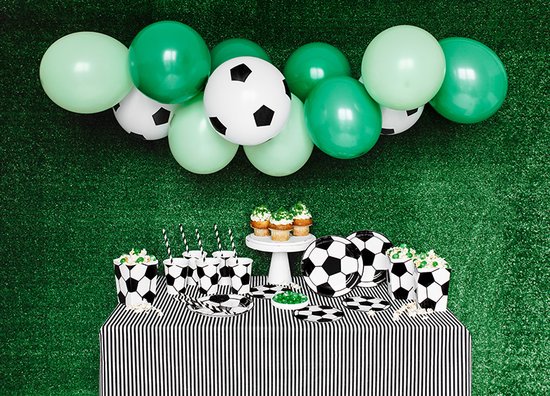 Groene en voetbalvormige ballonnen boven een tafel met zwart-wit gestreepte tafelkleed en voetbalthema servies.