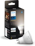 Verpakking van een Philips Hue White GU10 spotje. Naast de verpakking ligt het witte spotje. Tekst op de verpakking: 'Philips Hue white', 'GU10', '400', 'works with Alexa', 'works with Google Assistant', 'Bluetooth', 'Zigbee'.