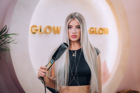 Une femme aux longs cheveux blonds raides avec des reflets tient un fer à lisser Sansbeauté noir.