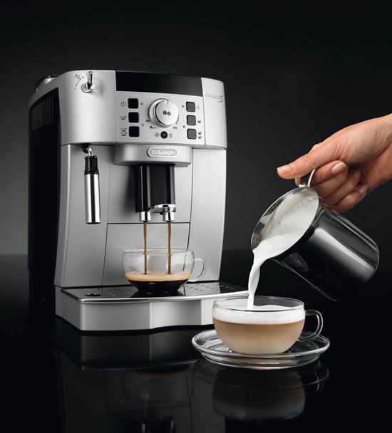 Zilverkleurige volautomaat schenkt espresso in twee glazen kopjes terwijl melk wordt opgeschuimd.
