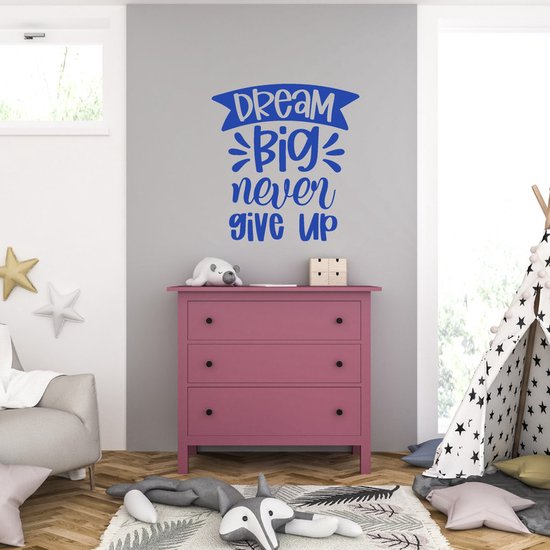 Blauwe muursticker met de tekst 'Dream Big never give up' in speelse letters op een grijze muur boven een roze commode.