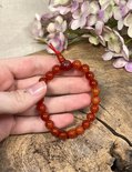 Hand met oranje carneool kralenarmband met rode draad