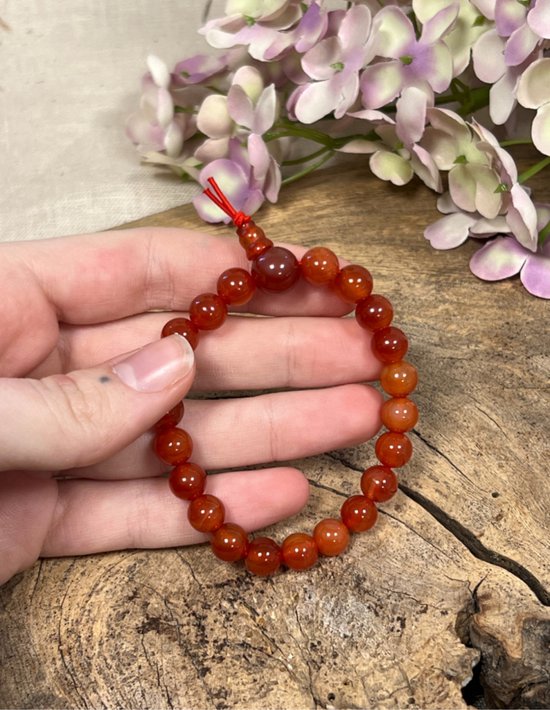 Hand met oranje carneool kralenarmband met rode draad