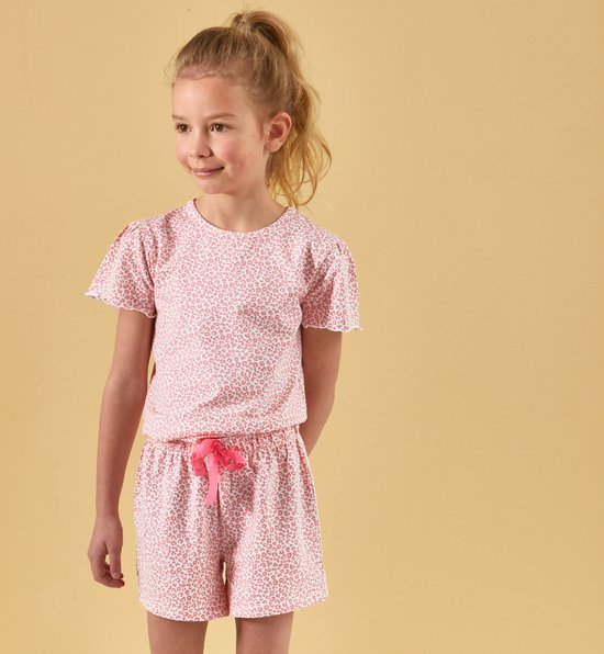 Une jeune fille avec une queue de cheval, portant un pyjama rose à imprimé léopard, composé d'un t-shirt et d'un short.