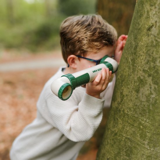 Jongen met een witte trui kijkt door een groene en witte periscoop naast een boom.