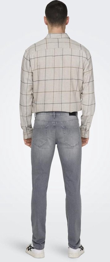 Man in lichtgrijs gewassen spijkerbroek met slim fit. Draagt een beige geruit overhemd.