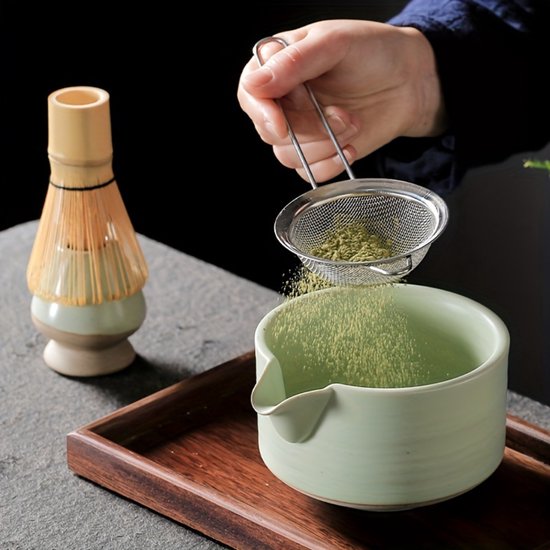 Groene matcha kom wordt gevuld met matcha poeder uit een metalen zeef, met klopper.