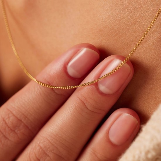 Close-up van een gouden gourmet ketting van 1 mm breed, gedragen om de nek, met vingers die de ketting aanraken.