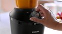 Hand draait aan de knop van een zwarte Philips blender met oranje vloeistof.