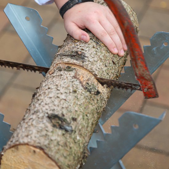 Een hand zaagt met een handzaag een boomstam door op een metalen zaagbok.