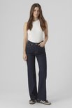 Model met donkerblauwe spijkerbroek met wijde pijpen en hoge taille, gedragen met wit topje.