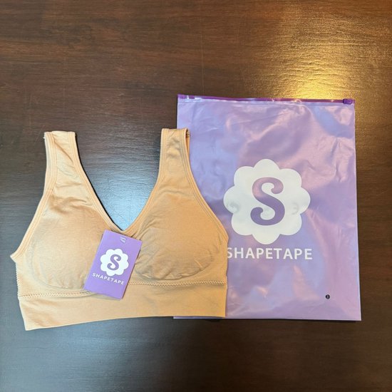 Soutien-gorge beige sans couture avec étiquette 'SHAPETAPE' à côté d'un sac d'emballage violet.
