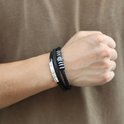 Zwarte leren armband met RVS accenten, gedragen om een pols.