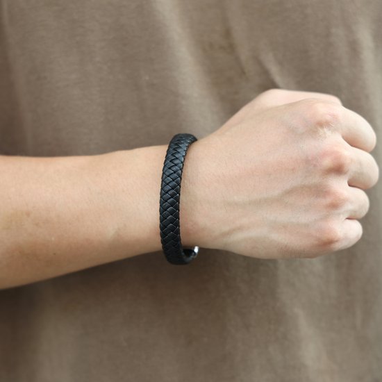 Zwarte gevlochten leren armband met zilverkleurige sluiting, gedragen om een pols.