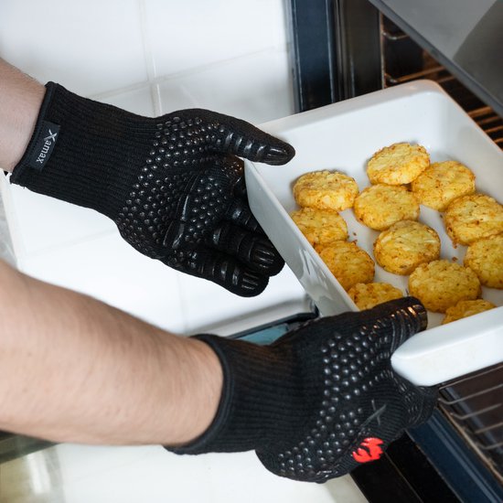 Handen met zwarte, hittebestendige handschoenen met siliconen noppen halen een ovenschotel uit de oven.