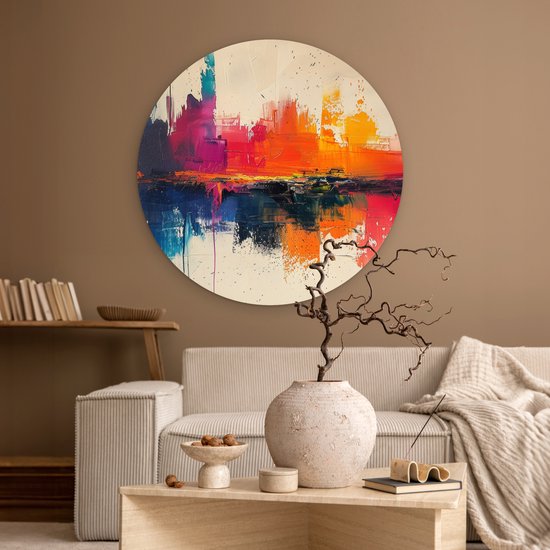 Abstracte muurcirkel met felle kleuren in een woonkamer met beige bank en salontafel.