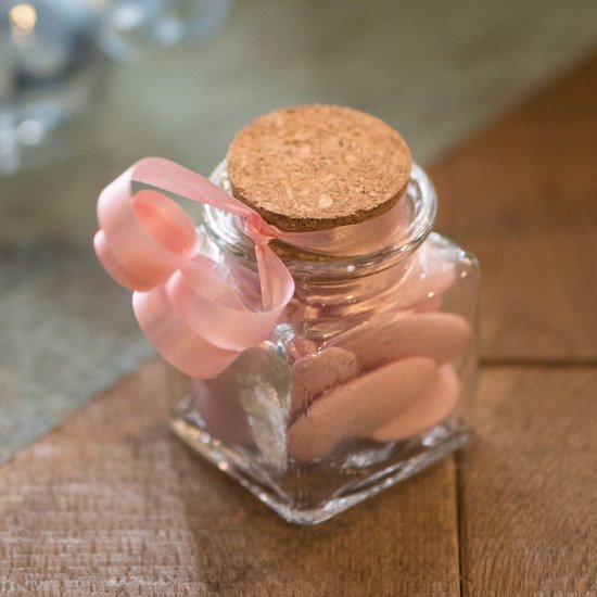 Petite bouteille carrée en verre avec bouchon en liège, remplie de bonbons roses en forme de cœur, décorée d'un ruban rose.