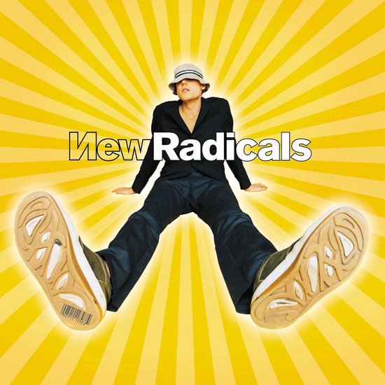 Een persoon met een hoed zit met gespreide benen op een gele achtergrond met uitstralende lijnen. Ze dragen een zwart jasje en broek.