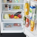 Binnenkant van een open koelkast met groenten, fruit, zuivel, frisdrank en saus.