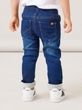 Achterkant van een jongetje in een donkerblauwe spijkerbroek met stonewashed effect, trekkoord en oranje stiksels. Omgeslagen broekspijpen.