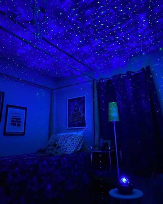 Een slaapkamer met blauwe sterren geprojecteerd op het plafond door een sterrenprojector. Een bed en een nachtkastje zijn zichtbaar.