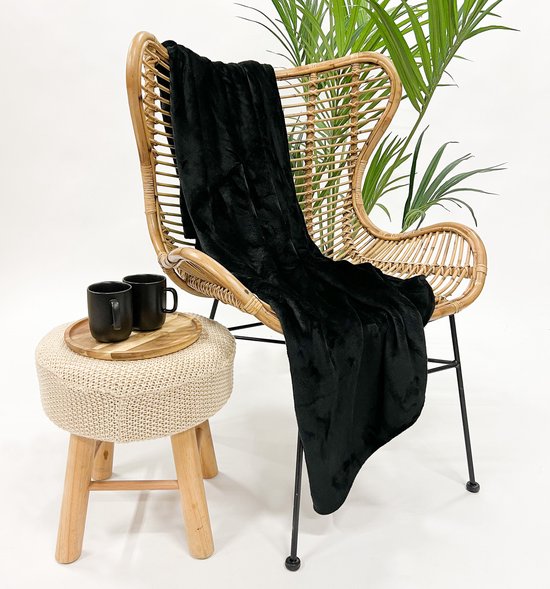 Een zwart fleece plaid over een rotan stoel met een klein krukje met mokken ernaast.