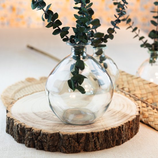 Twee glazen vazen met eucalyptus takjes op houten boomschijf.