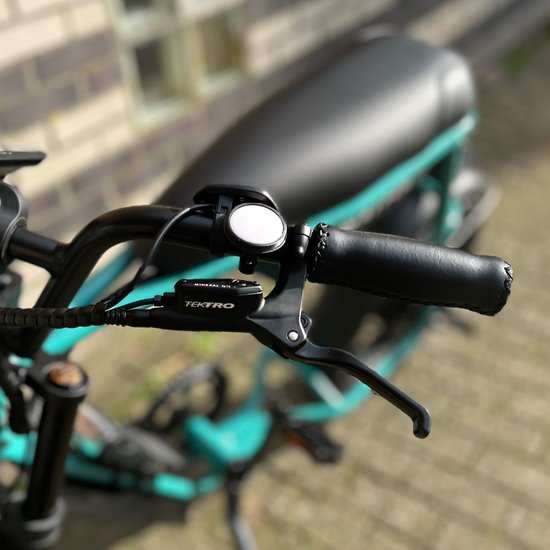 Zwarte fietsbel met AirTag houder op het stuur van een turquoise elektrische fiets met zwarte handvatten.