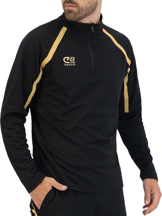 Een man draagt een zwarte Cruyff trainingssweater met gouden accenten op de schouders en een half-zip.