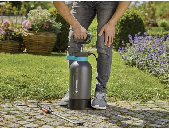 Persoon met grijze jeans en sneakers drukt op de pomp van een donkergrijze 5L drukspuit met turquoise accenten.