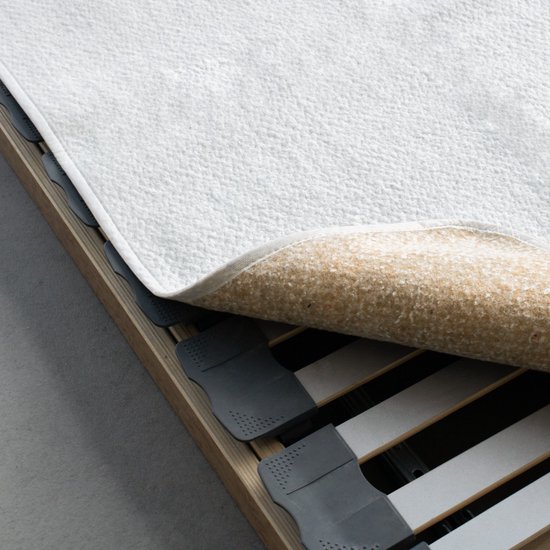 Een matrasbeschermer met een witte bovenkant en een beige onderkant, op een houten bedbodem met zwarte flexibele latten.