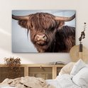 Glasafbeelding van een bruine Schotse hooglander met grote hoorns, hangend boven een bed.